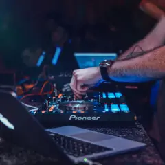 DJ obsługujący mikser Pioneer i laptopa, z podświetleniem niebieskim i czerwonym.