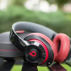 Czarne i czerwone słuchawki bezprzewodowe Beats Studio leżą obok etui na ławce. Idealne, jeśli zastanawiasz się, jakie słuchawki bezprzewodowe wybrać.