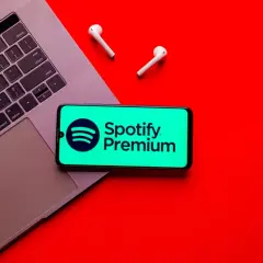 Telefon z logo Spotify Premium na tle laptopa i słuchawek bezprzewodowych.