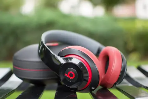 Czarne i czerwone słuchawki bezprzewodowe Beats Studio leżą obok etui na ławce. Idealne, jeśli zastanawiasz się, jakie słuchawki bezprzewodowe wybrać.