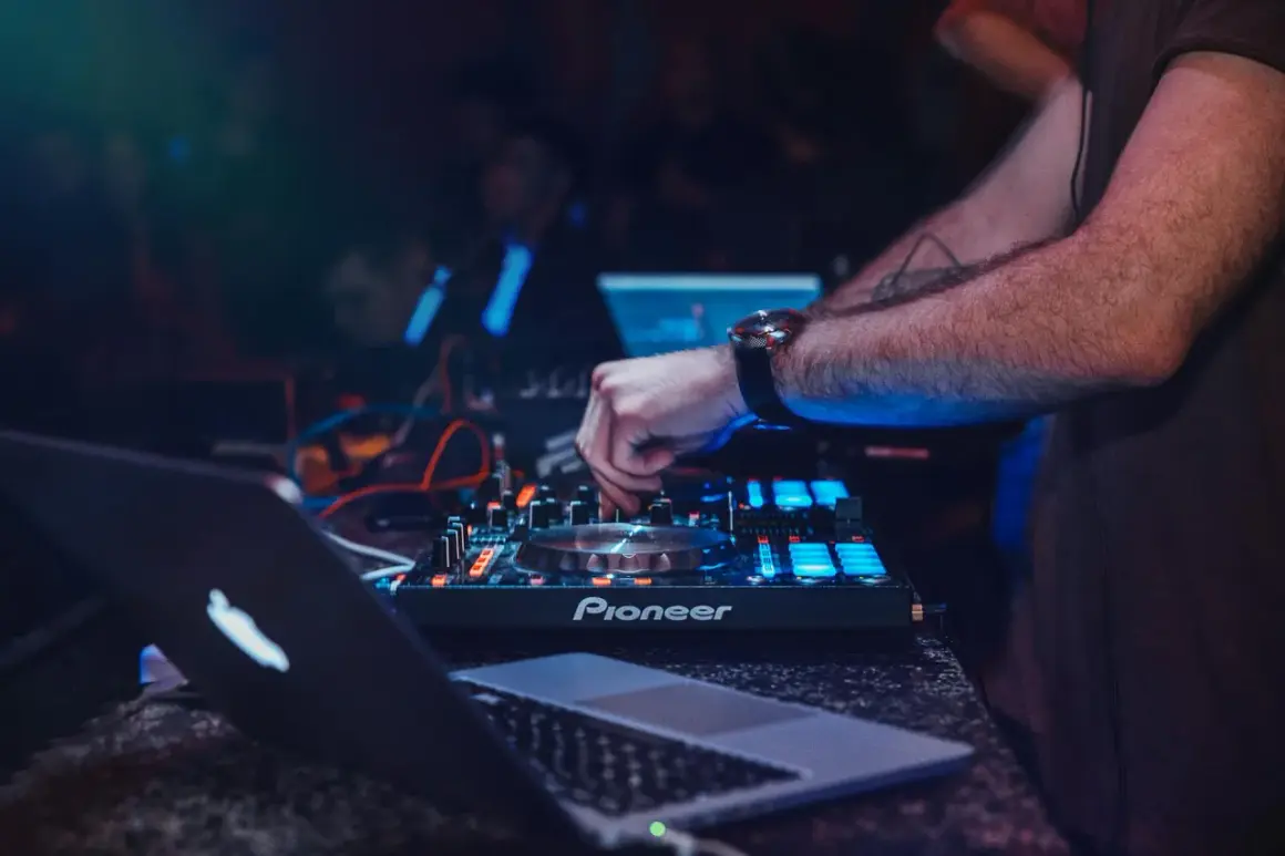 DJ obsługujący mikser Pioneer i laptopa, z podświetleniem niebieskim i czerwonym.