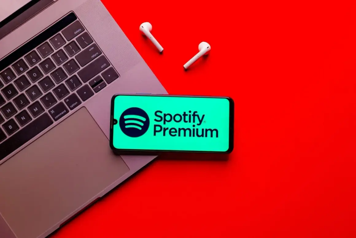 Telefon z logo Spotify Premium na tle laptopa i słuchawek bezprzewodowych.