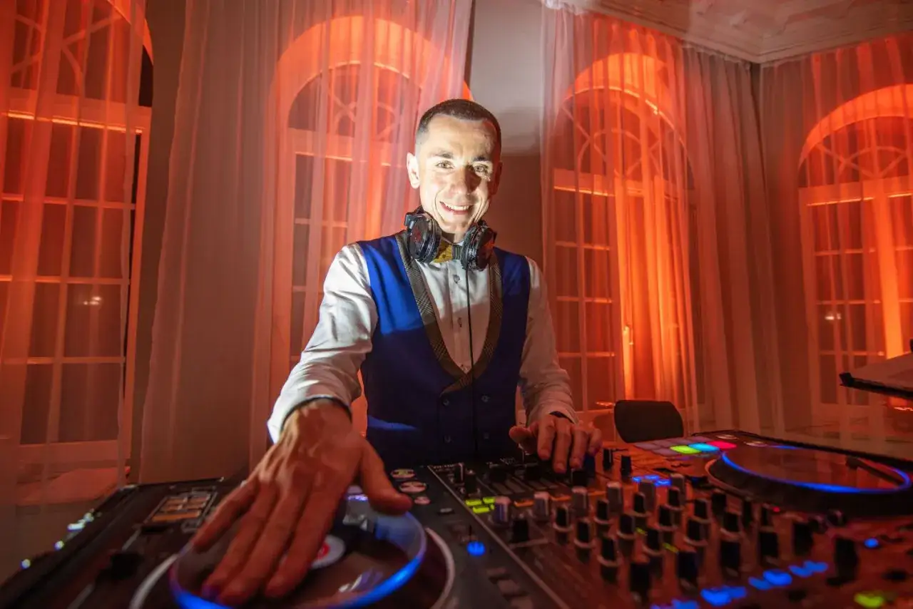 Uśmiechnięty DJ przy konsoli, gotowy do imprezy. Zastanawiasz się, ile kosztuje dj na imprezę?