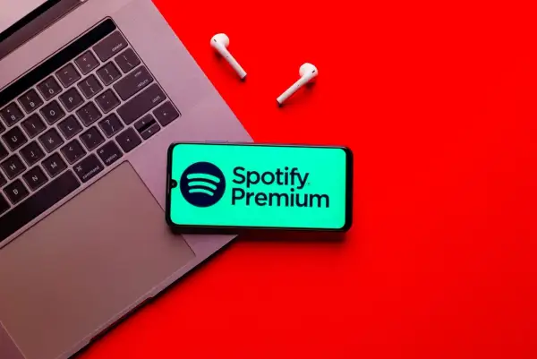 Telefon z logo Spotify Premium na tle laptopa i słuchawek bezprzewodowych.